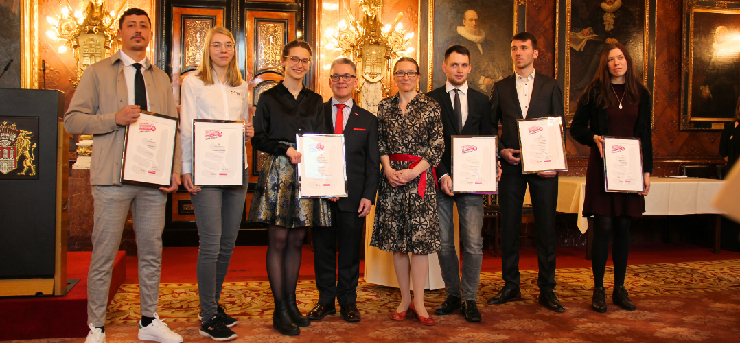 Drei junge Männer und drei junge Frauen stehen mit Urkunden in der Hand in einer Reihe. In Ihrer Mitte stehen der Präsident der Handwerkskammer, Hjalmar Stemmann und die Senatorin für Schule und Berufsbildung Ksenija Bekeris. Der Hintergrund ist der prunkvolle Bürgermeistersaal im Hamburger Rathaus.